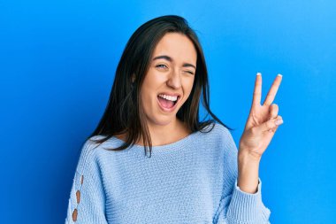 Gündelik kıyafetler giyen, gülümseyen ve kameraya göz kırpan genç İspanyol kız zafer işareti yapıyor. İki numara.. 