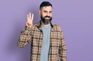 Hispanic man with beard wearing casual shirt showing and pointing up with fingers number three while smiling confident and happy. 
