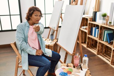 Resim stüdyosunda resim yapan orta yaşlı bir kadın kamerayı işaret ederek resim yapıyor ve sen kendine güvenen ciddi bir hareket yapıyorsun. 