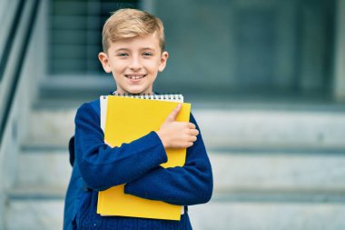 Sevimli sarışın öğrenci gülümseyerek okulda mutlu bir şekilde kitap tutuyor..