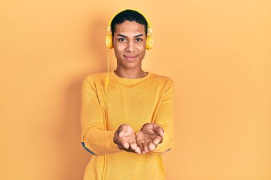 Genç Afro-Amerikalı adam müzik dinliyor kulaklıkla gülümsüyor, avuç içleriyle gülümsüyor ya da el hareketi yapıyor. Bekleme ve koruma 