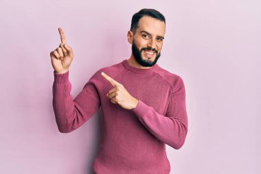 Sakallı genç adam, sıradan bir kazak giyiyor gülümsüyor ve kameraya bakıyor.. 