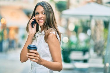 Güzel Latin genç kız akıllı telefondan konuşuyor ve şehirde kahve içiyor..