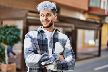 Genç İspanyol adam mutlu bir şekilde gülümsüyor şehirde çapraz hareketlerle.