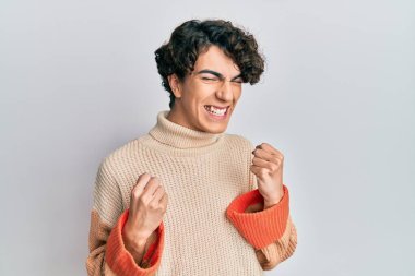 Sıradan bir kazak giyen İspanyol genç adam başarı için heyecanlı kolları havada ve gözleri kapalı zaferi kutlarken gülümsüyor. Kazanan konsept. 