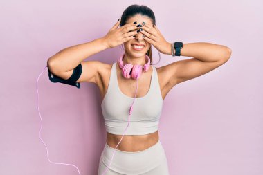 Spor kıyafetleri giyen, kulaklık takan, gözleri kapayan neşeli ve komik gülümseyen İspanyol bir kadın. kör kavram. 