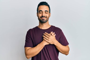 Gündelik kıyafetler giyen genç İspanyol adam elleri göğsünde gülümsüyor, gözleri kapalı ve yüzünde minnet ifadesi var. sağlık kavramı. 