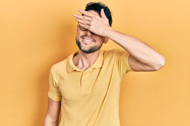 Gündelik kıyafetler giyen, gözlüklü, gülümseyen ve gülümseyen genç İspanyol adam şaşırmak için gözlerini kapatıyor. kör kavram. 