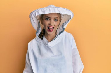 Sarışın, beyaz, koruyucu arı üniforması giyen güzel bir kadın komik bir ifadeyle dilini dışarı çıkarıyor. duygu kavramı. 