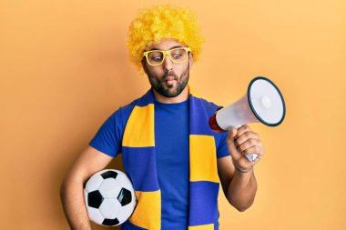 Genç İspanyol futbolcu futbol taraftarı futbol topu tutuyor megafon kullanıyor balık suratlı ve şaşı gözlü, çılgın ve komik.. 