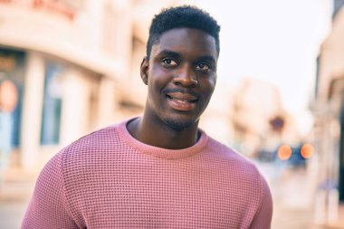 Genç Afrikalı Amerikalı adam gülümseyerek şehirde mutlu mesut duruyor..