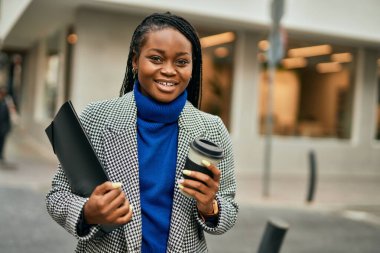 Genç Afrikalı Amerikalı iş kadını gülümseyerek şehirde kahve içiyor..