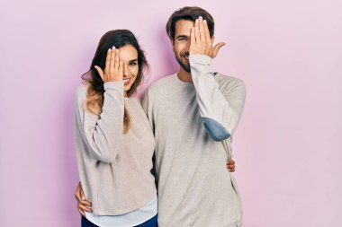 Genç İspanyol çift gündelik kıyafetler giyip bir gözünü eliyle kapatıyor, yüzünde kendine güvenen bir gülümseme ve sürpriz bir duygu var.. 