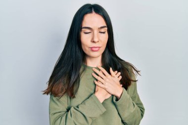 Genç esmer kadın, gündelik yeşil süveter giyiyor. Elleri göğsünde, gözleri kapalı gülümsüyor ve yüzünde minnet ifadesi var. sağlık kavramı. 