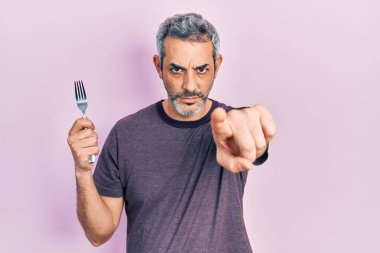 Gri saçlı, gümüş çatallı, kamerayı işaret eden yakışıklı, orta yaşlı bir adam. Kendine güvenen, ciddi görünen bir jest. 