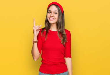 Genç esmer kadın gündelik kıyafetler giyip bir numarayı gösterip işaret ederken kendinden emin ve mutlu bir şekilde gülümsüyor.. 