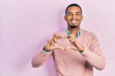 Zarif giysiler giymiş genç Afro-Amerikan bir adam. Sevgiyle gülümsüyor. Elleriyle kalp sembolü ve şekli gösteriyor. romantik kavram. 