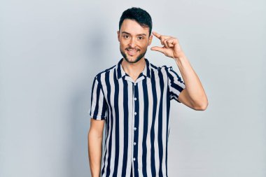 Gündelik kıyafetler giyen, gülümseyen, kendine güvenen, el hareketi yapan, parmaklarıyla işaret yapan ve kameraya bakan genç İspanyol bir adam. ölçüm kavramı. 