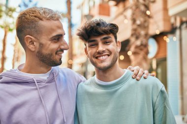 Mutlu bir şekilde gülümseyen ve şehirde sarılan genç eşcinsel çift..
