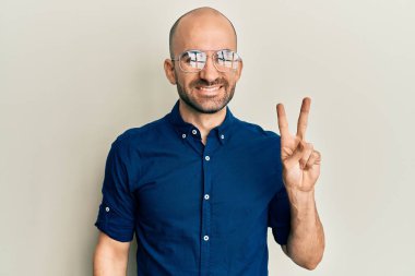 Gündelik kıyafetler ve gözlük takan genç İspanyol adam kameraya gülümseyip zafer işareti yapıyor. İki numara.. 