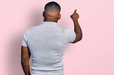 Gündelik tişört giyen genç siyahi adam tersten öne doğru parmak ile poz veriyor. 