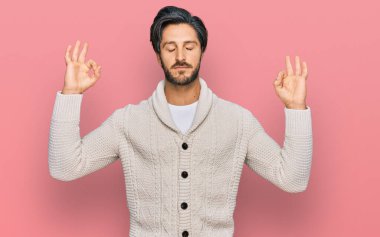 Günlük kıyafetler giyen genç İspanyol adam rahatla ve gözleri kapalı gülümse parmaklarıyla meditasyon hareketi yapıyor. yoga konsepti. 