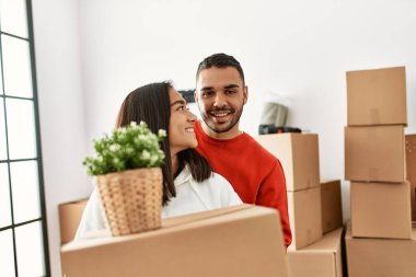 Genç Latin çift mutlu bir şekilde gülümsüyor. Yeni evlerinde karton kutu tutuyorlar..