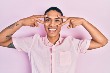 Genç Afro-Amerikalı adam zafer işareti yapıyor ve yüzünde mutlu ve havalı bir gülümsemeyle barış jesti yapıyor. diş gösterme. 