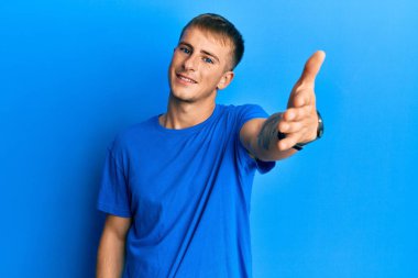 Sıradan mavi tişörtler giyen genç beyaz bir adam dostça bir selamlama ve hoş geldin hediyesi olarak el sıkışmayı teklif ediyor. başarılı iş. 