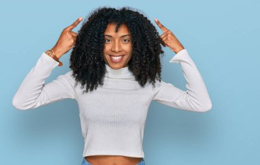 Gündelik giysiler giymiş genç Afro-Amerikalı kız iki eliyle başını gösteren gülümseme, harika fikir ya da düşünce, iyi hafıza 