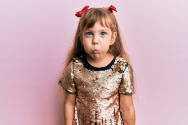 Şenlikli pullar giyen beyaz bir kız çocuğu komik yüzüyle yanaklarını şişiriyor. Havayla şişmiş ağız, çılgın bir ifade.. 