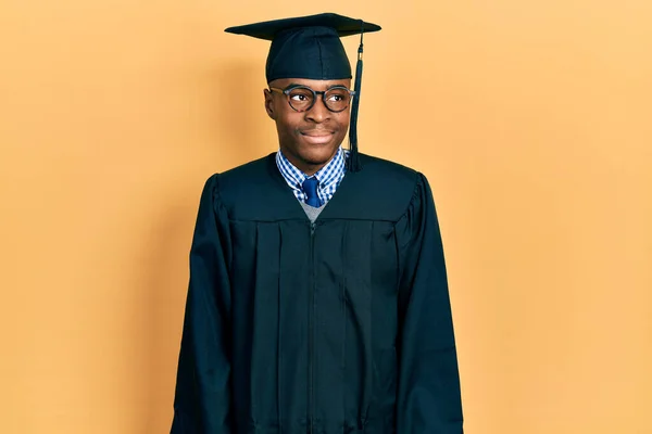 年轻的非洲裔美国人头戴毕业典礼帽 身穿礼袍 面带微笑地向旁边看去 目不转睛地想着 — 图库照片
