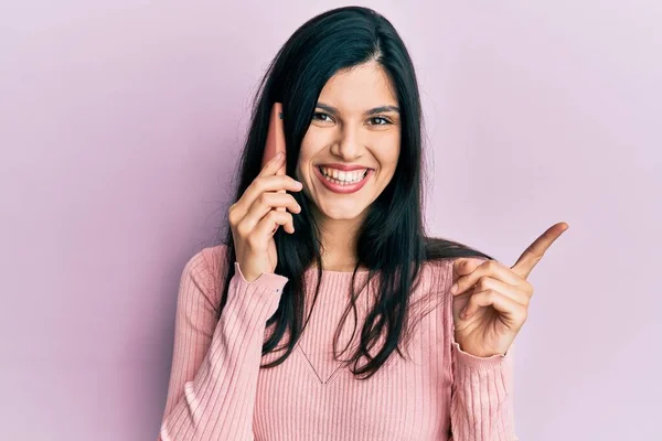 側に手と指を指して幸せな笑顔のスマートフォンで話している若いヒスパニック系の女性 — ストック写真