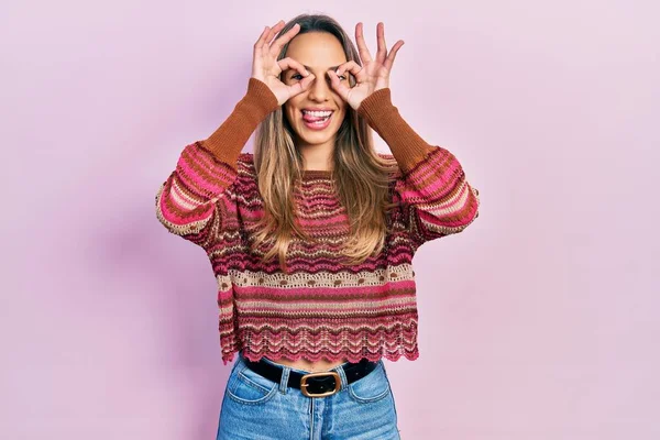 美しいヒスパニック系の女性は 双眼鏡の舌を突き出すようなOkジェスチャーを行うヒッピーセーターを着て 目の指を見て クレイジーな表現 — ストック写真