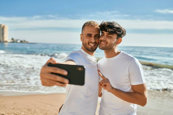 在海滩上 一对年轻的同性恋夫妇一边笑着一边用智能手机自拍 — 图库照片