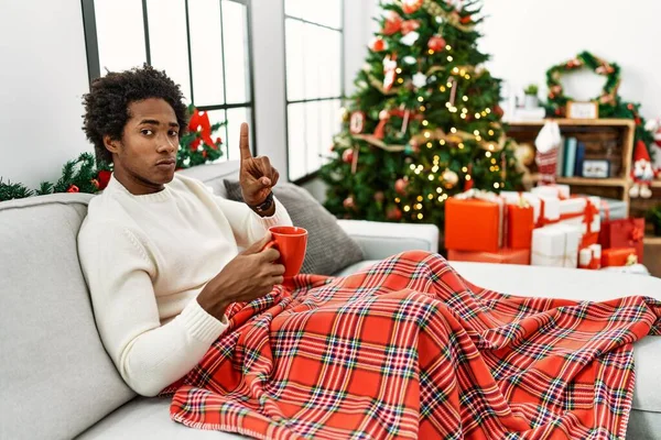Joven Afroamericano Sentado Sofá Bebiendo Café Junto Árbol Navidad Señalando — Foto de Stock