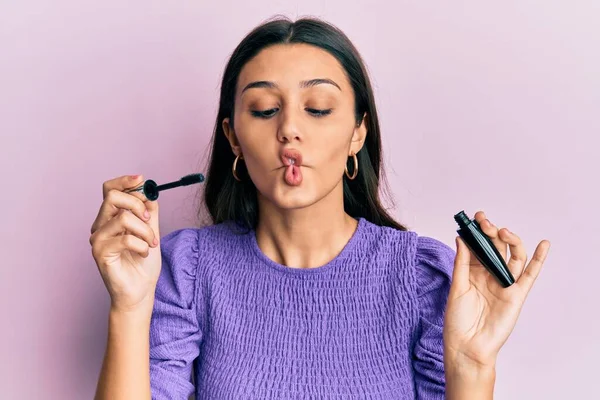 Young hispanic woman holding eyelashes curler making fish face with mouth and squinting eyes, crazy and comical.