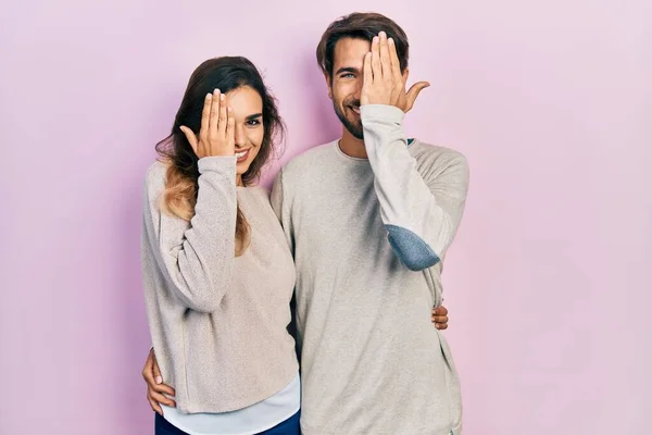 若いヒスパニック系のカップルは 手で一つの目をカバーカジュアル服を着て 顔に自信を持って笑顔と驚きの感情 — ストック写真