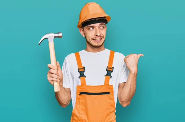 Joven Hispano Con Sombrero Fuerza Sosteniendo Martillo Señalando Pulgar Hacia — Foto de Stock