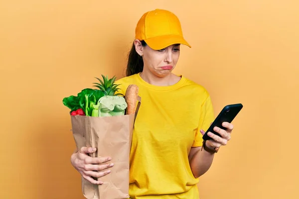 Ung Latinamerikansk Kvinna Håller Påse Livsmedel Med Smartphone Deprimerad Och — Stockfoto