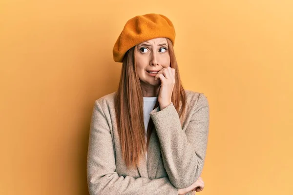 Young irish woman wearing french look with beret looking stressed and nervous with hands on mouth biting nails. anxiety problem.