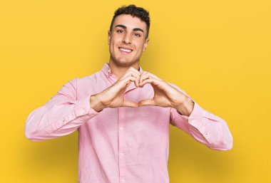 Gündelik kıyafetler giyen İspanyol genç bir adam. Sevgiyle gülümsüyor. Kalp sembolü ve elleri ile şekil veriyor. romantik kavram. 