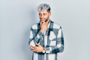 Modern boyalı saçlı, elleri çenesinde gündelik tişörtler giyen soru soran, düşünceli bir İspanyol genç. Düşünceli bir yüzle gülümsüyor. şüphe kavramı. 