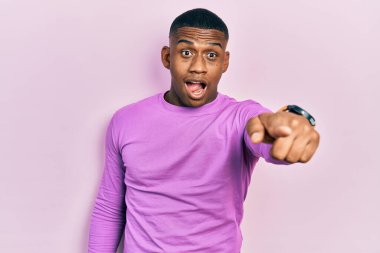 Genç siyah bir adam pembe bir süveter giyiyor. Parmağıyla işaret ediyor. İleriyi işaret ediyor. 