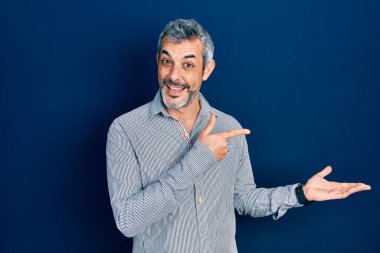 Gri saçlı, iş gömleği giyen yakışıklı orta yaşlı bir adam hayrete düşmüş ve kameraya gülümsüyor.. 