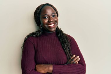 Sıradan kıyafetler giyen Afrikalı genç bir kadın kollarını kavuşturup kameraya bakarak gülümsüyor. pozitif kişi. 