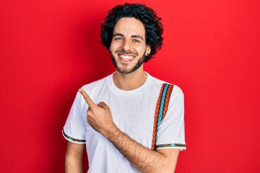 Yakışıklı İspanyol adam mutlu ve havalı bir gülümsemeyle parmaklarını yana doğru gösteriyor. diş gösterme. 