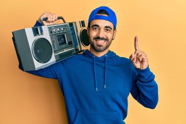 Latin asıllı genç adam elinde teyp ile müzik dinlerken bir fikir ya da soruyla şaşırmış ve mutlu bir yüzle işaret ediyor. 