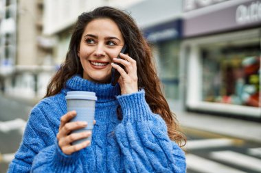 Genç İspanyol kadın akıllı telefondan konuşuyor ve şehirde kahve içiyor..