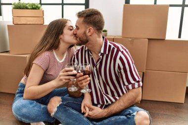 Kafkasyalı genç çift kırmızı şarapla kadeh kaldırıyor ve yeni evinde öpüşüyor.